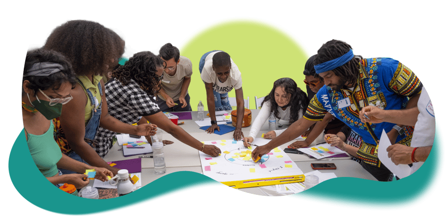 A number of people work together around a table. They are putting together are chart with brightly colored sticky notes, and writing on it.