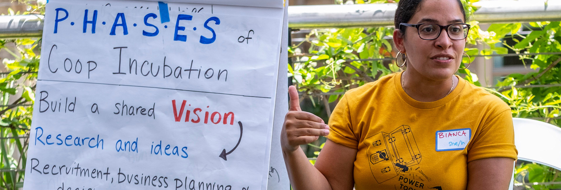 A person sits next to a chart, and appears to be mid sentence. The chart reads some information about co-op incubation. A person sits next to a chart, and appears to be mid sentence. The chart reads some information about co-op incubation.